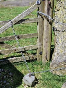 gravity based self closing hinge with a chain and stone attached to a gate in the countryside