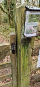 Black keyless keypad digital gate lock on weathered wooden gate and fence in private estate area.