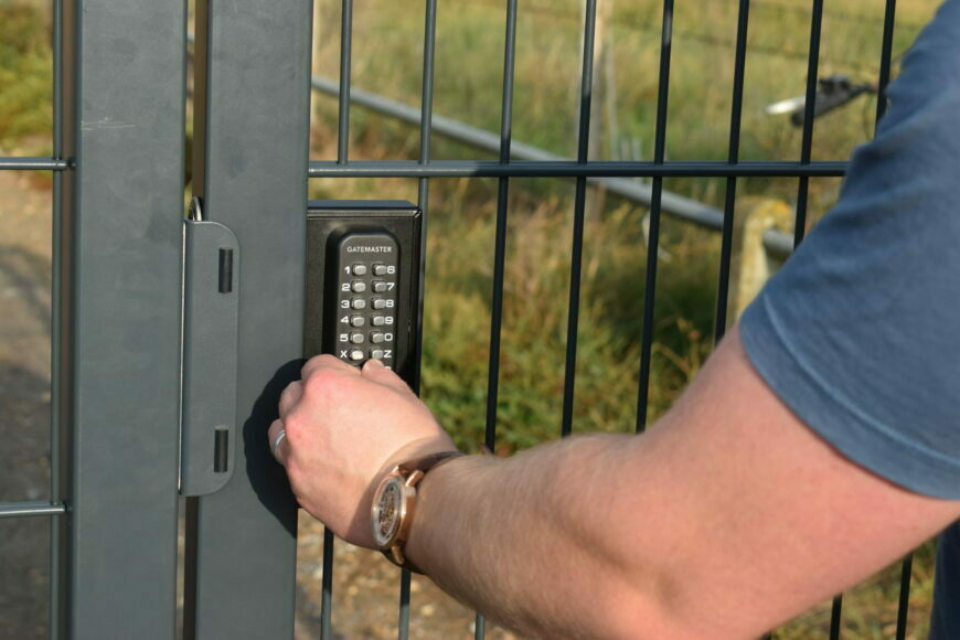 Picture of person punching in a code on a digital keypad lock on a grey metal gate