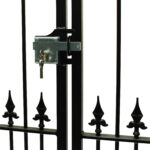Exterior gate lock bolted on black metal gate with ornamental spears at bottom rail. lock is deadbolted and has a set of keys hanging from euro cylinder