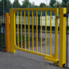 Yellow metal pedestrian gate at leisure centre with self-closing gate hinge on bottom hinge and pivoting top hinge