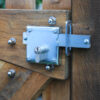 Shiny metal locking bolt with key cylinder and square bolt secured on a wooden garden gate with wood screws. Bolt going through locking plate