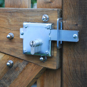 Shiny metal locking bolt with key cylinder and square bolt secured on a wooden garden gate with wood screws. Bolt going through locking plate