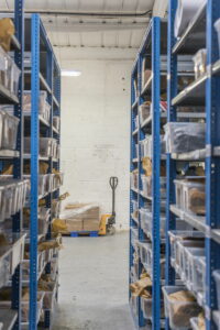 Two blue warehouse racking systems on either side with view to a small pallet truck with boxes on in the middle