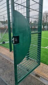 green metal gate with digi lock keypad in front of football field