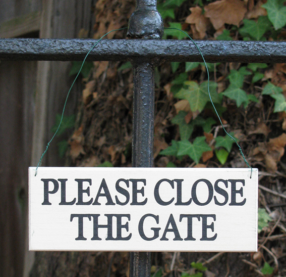Wrought iron gate with sign hanging with green metal wire. White sign with black text "Please close the gate"