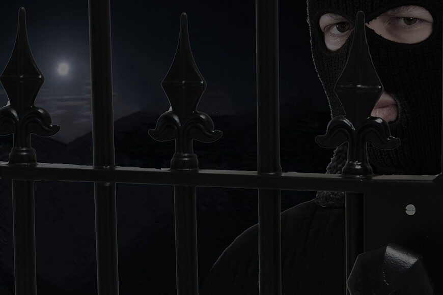 Black metal gate with weld in lock with octagon handle. Right behind is person with a skimask on. In background, night sky with full moon