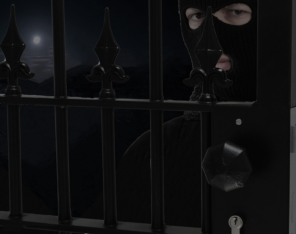 Black metal gate with weld in lock with octagon handle. Right behind is person with a skimask on. In background, night sky with full moon