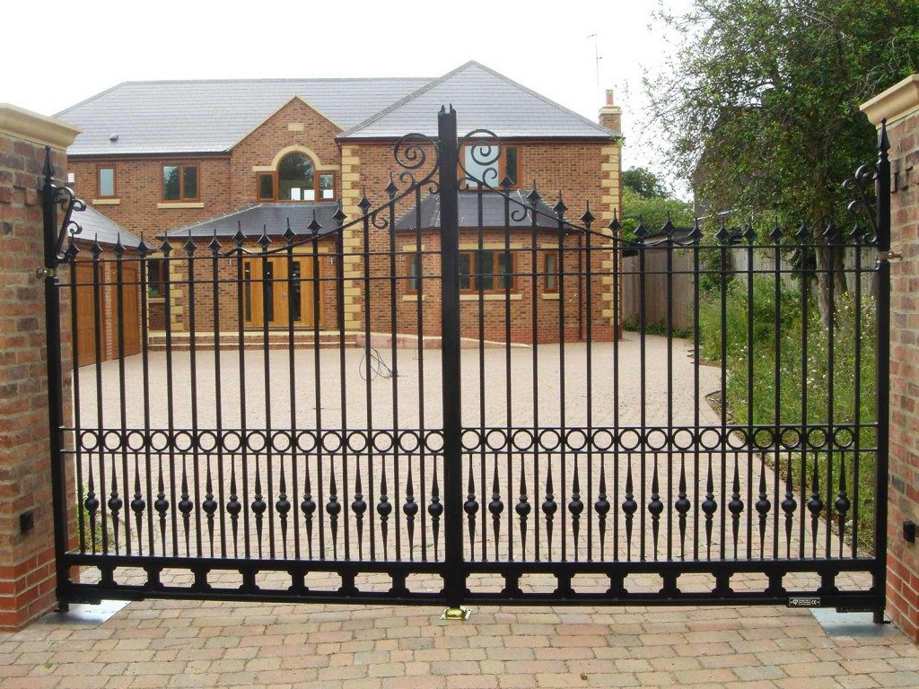 Ornamental metal gate with scroll work in front of a red brick house and driveway