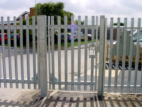 Commercial steel palisade pedestrian gate in front of parked cars and green with a tree